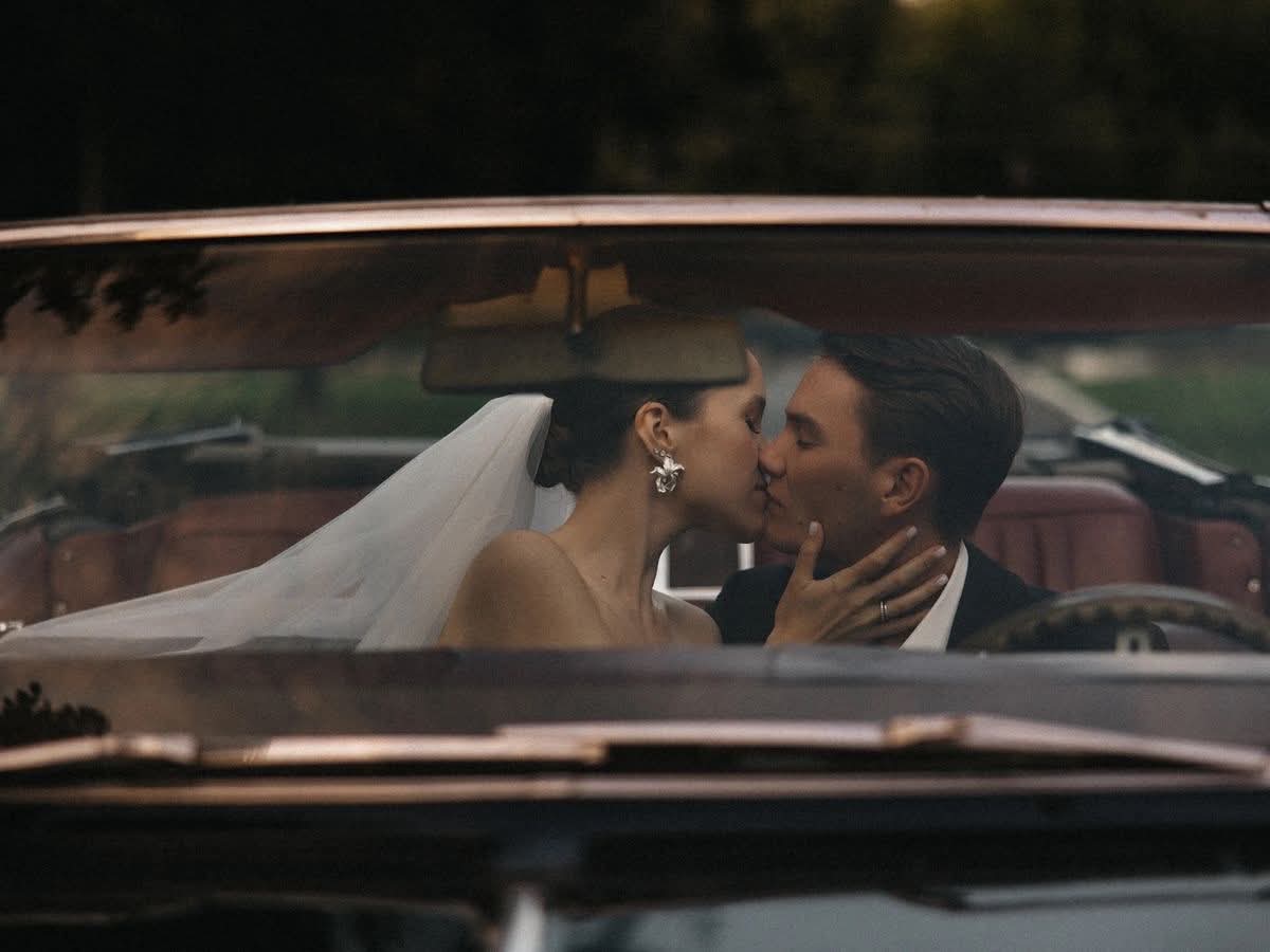 A bride and groom kissing in a vintage convertible.
